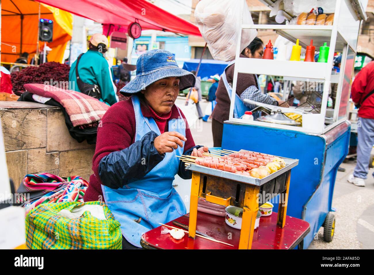 Puno, Bolivia - Jan 5, 2019: Unindentified donna in costume tradizionale rendendo un cibo sulla strada della città di Puno la città sul lago Titicaca, Bolivia. Foto Stock