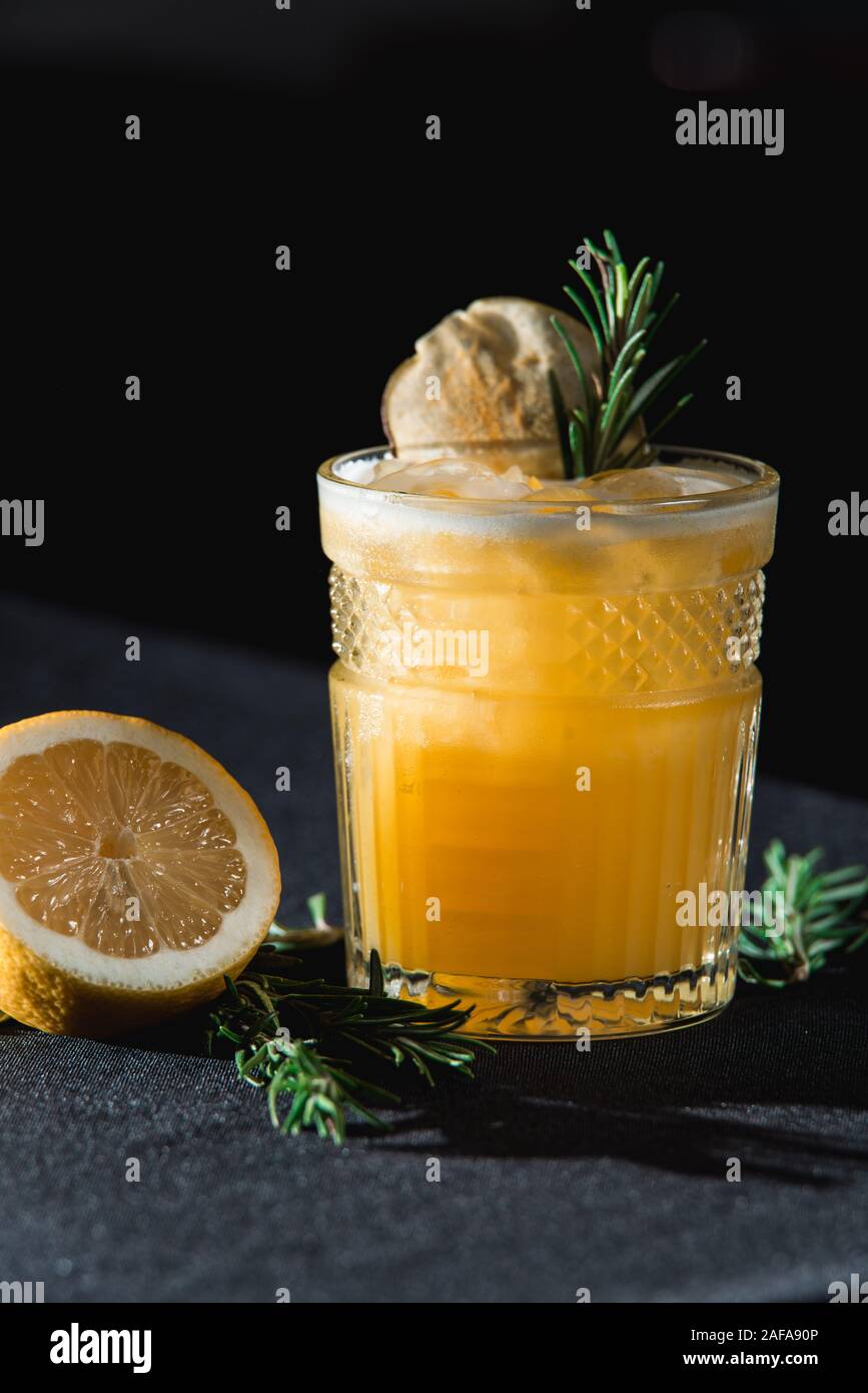 Il freddo Whiskey Sour cocktail con ghiaccio e chip di Apple e un pezzo di timo sulla parte superiore. La metà di un limone vicino al vetro Foto Stock