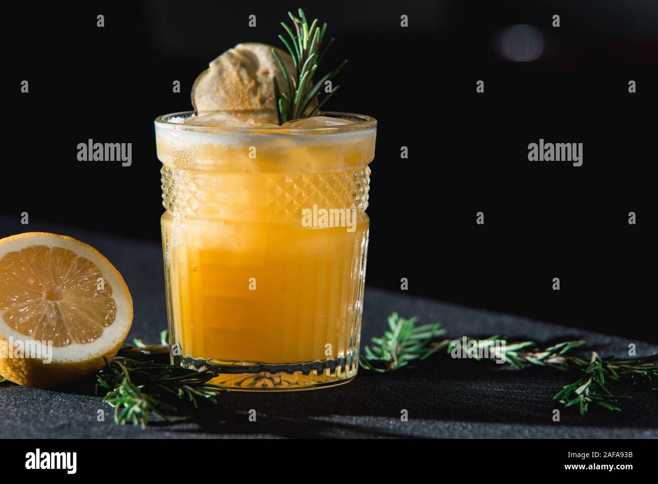 Il freddo Whiskey Sour cocktail con ghiaccio e chip di Apple e un pezzo di timo sulla parte superiore. La metà di un limone vicino al vetro Foto Stock