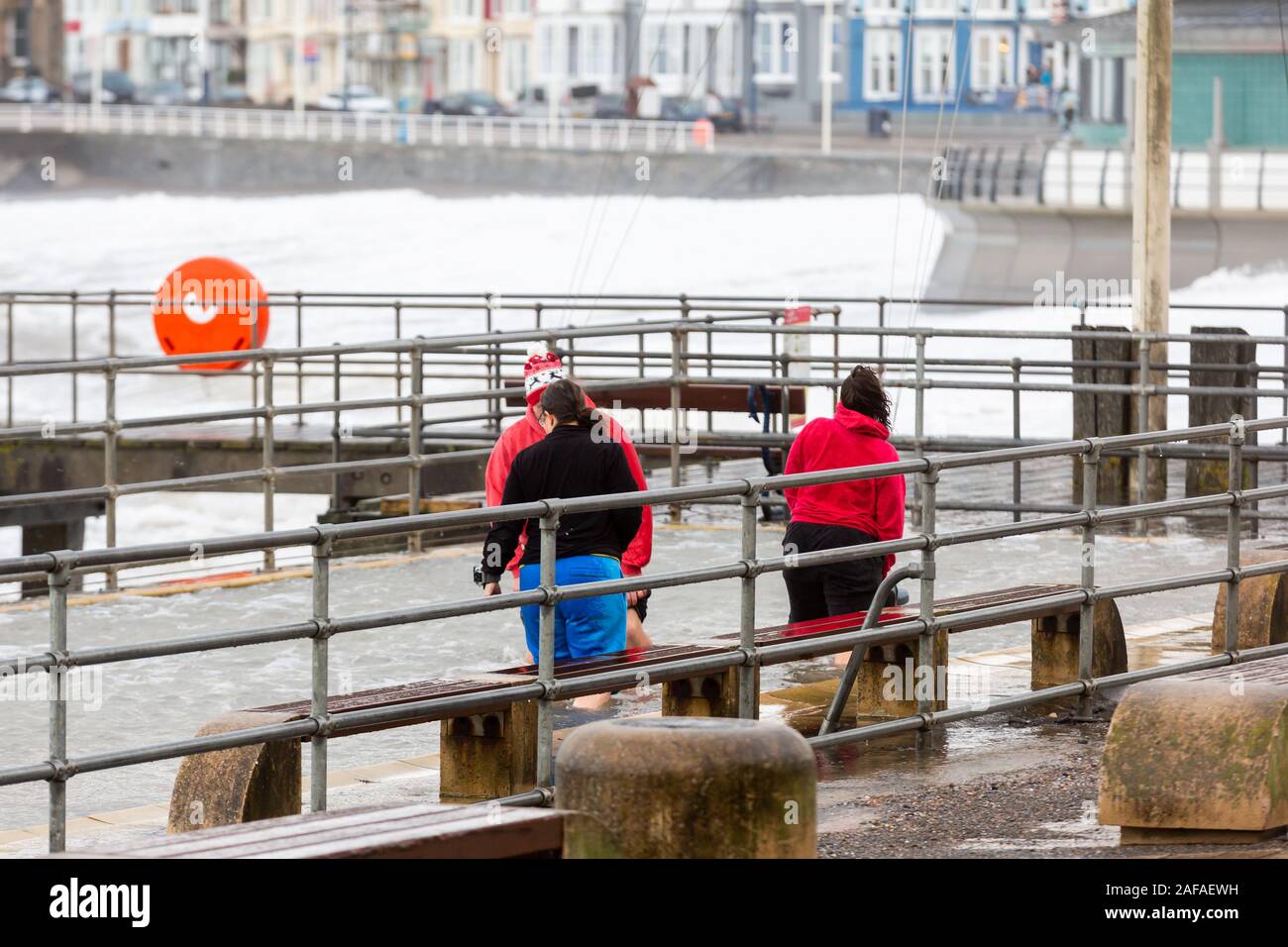 Aberystwyth, Ceredigion, Wales, Regno Unito. Xiv Dic, 2019. Regno Unito Meteo: Tre persone decidono di andare per una racchetta in passeggiata piscinetta per bambini come i venti forti e onde venire oltre il mare difese in Aberystwyth questa mattina. Credito: Ian Jones/Alamy Live News Foto Stock