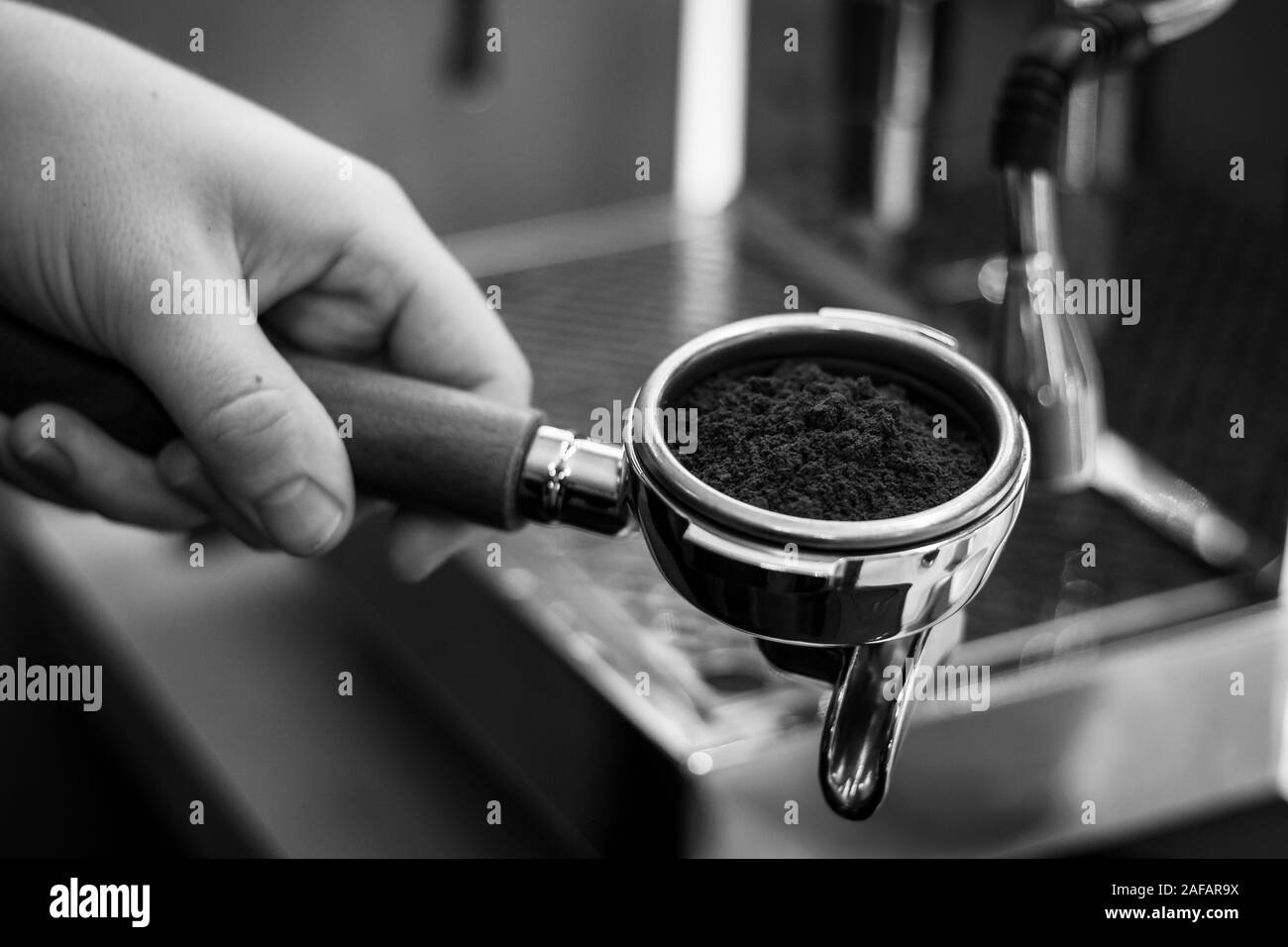Un ritratto in bianco e nero di un barista tenendo un caffè portafilter con caffè fresco motivi in esso pronta a fare alcuni caffè nella macchina da caffè. Foto Stock