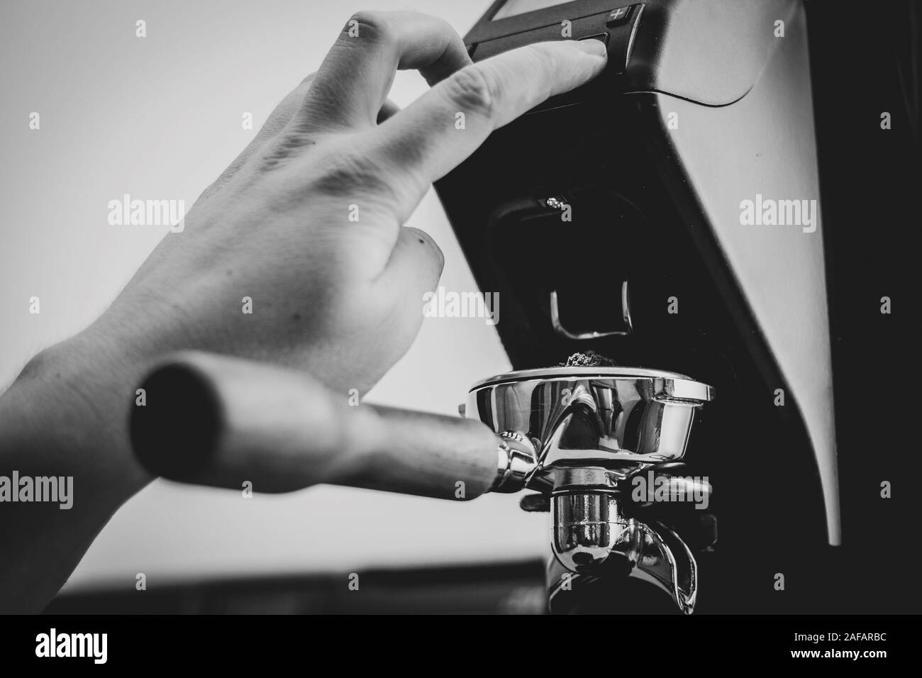 Un ritratto di un barista premendo il pulsante di un macinino da caffè per riempire un portafilter pieno di macinato di fresco caffè macinato fresco da chicchi di caffè. Foto Stock