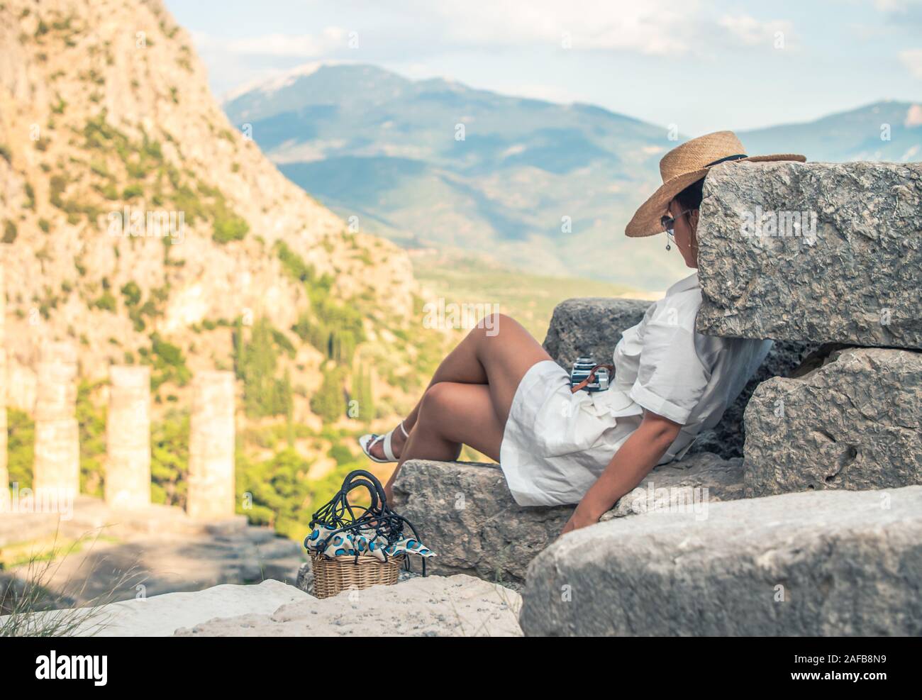 Giovane donna seduta turistici al Santuario di Athena, Delphi Grecia. Moda abito bianco, grandi hat, mantello giallo Foto Stock