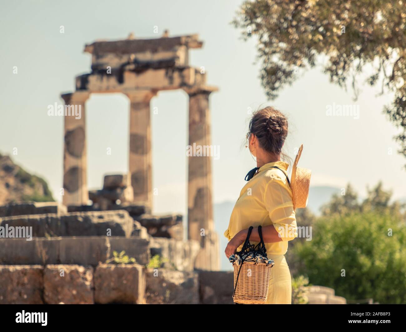 Giovane donna turista al Santuario di Athena, Delphi Grecia. Moda abito bianco, grandi hat, mantello giallo Foto Stock