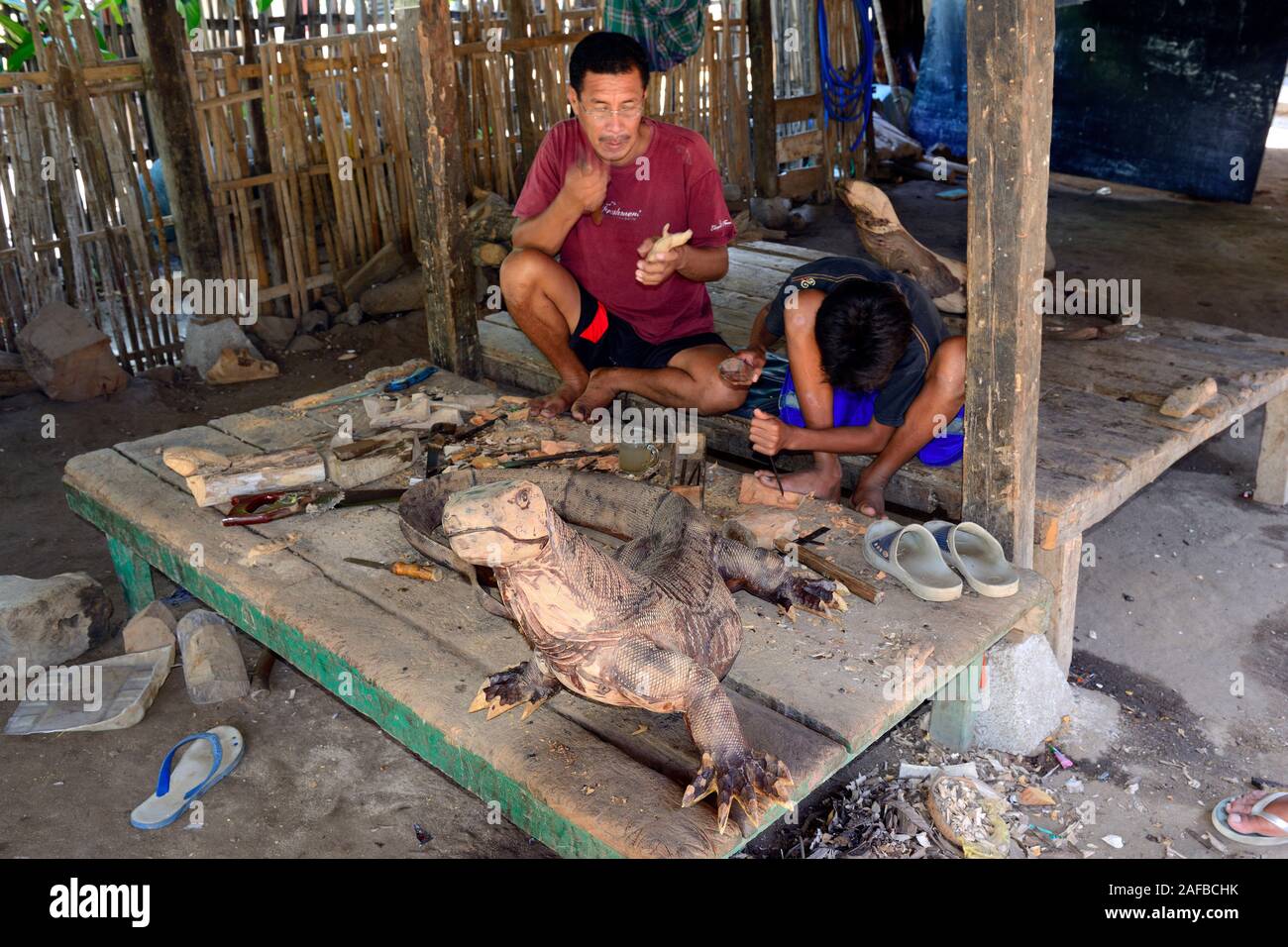 Vater und Sohn schnitzen unter ihrem Haus Komodowarane. Dorf Komodo, Komodo Nationalpark, Insel Komodo, UNESCO Welterbe , Indonesien Foto Stock