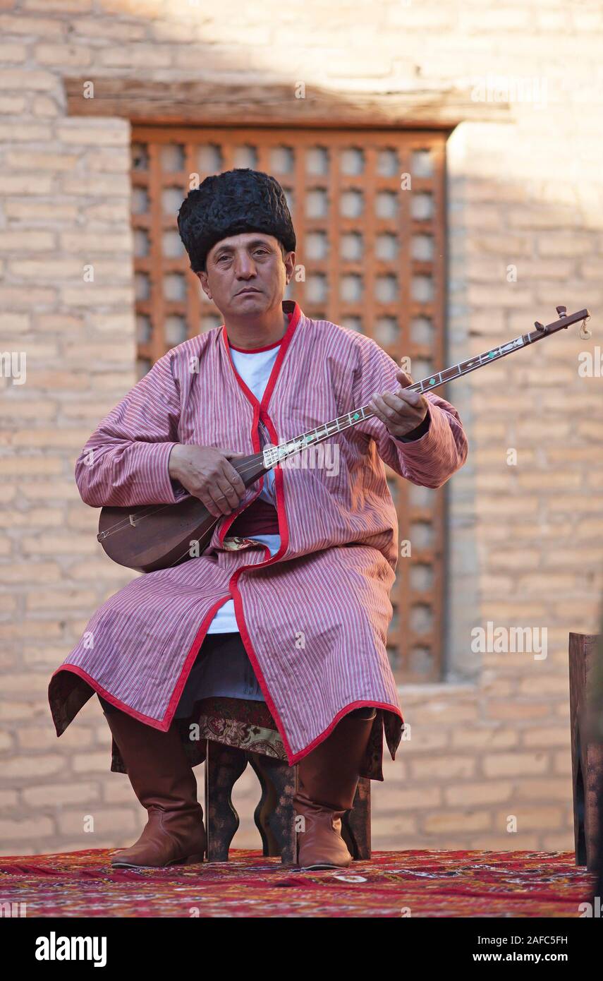 Uomo in costume tradizionale giocando sulla dombra, spennate tradizionale strumento, la città vecchia di Khiva, Provincia di Xorazm, Uzbekistan Foto Stock