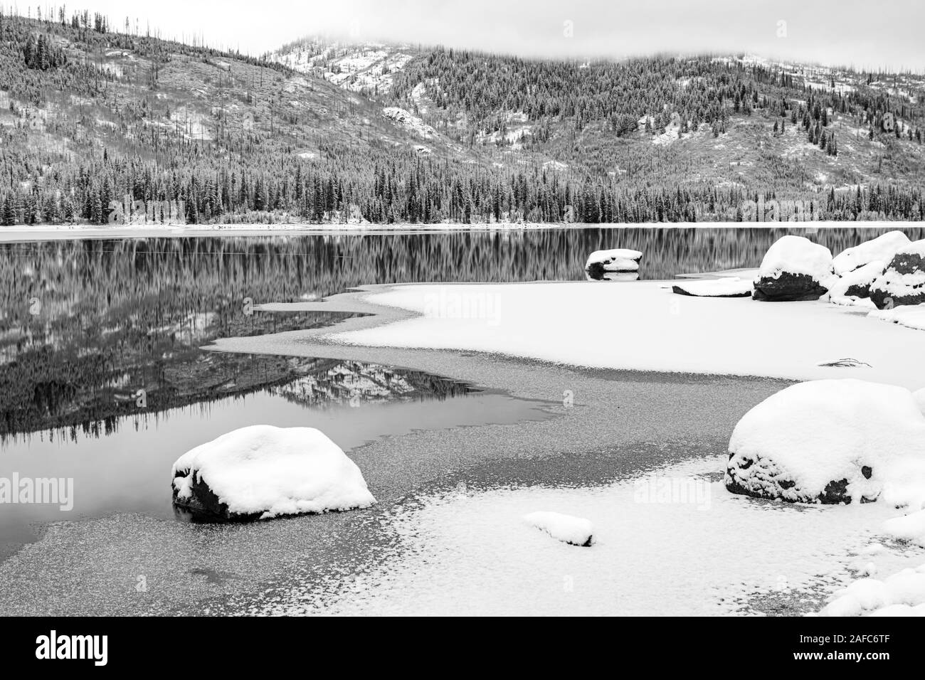 Ghiaccio e neve circondano un lago di montagna con la riflessione Foto Stock