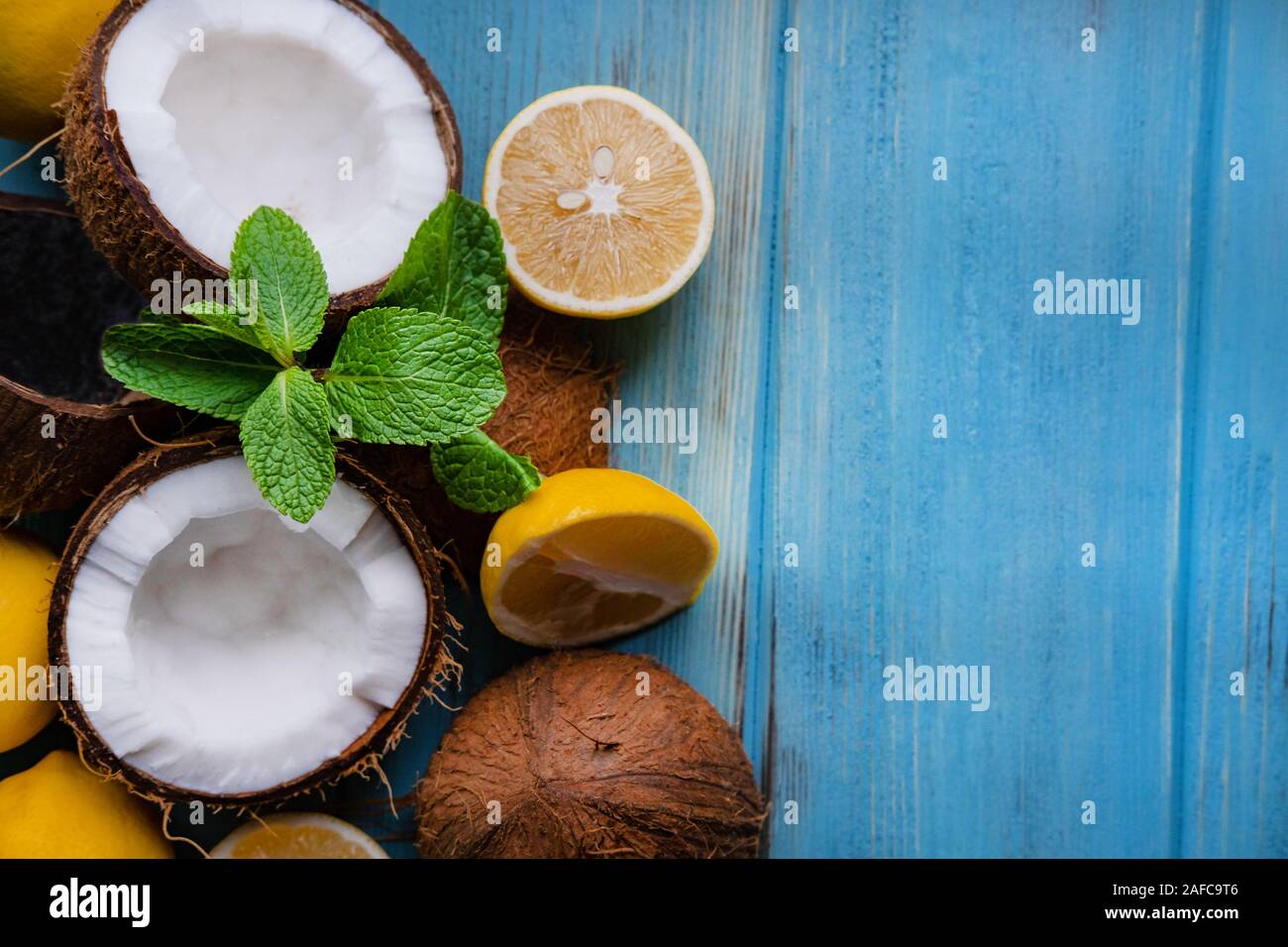 Tagliate le due metà di noce di cocco con limone e foglie di menta su un blu sullo sfondo di legno. Tropical sfondo esotico con noce di cocco Agrumi e posto per copiare spa Foto Stock