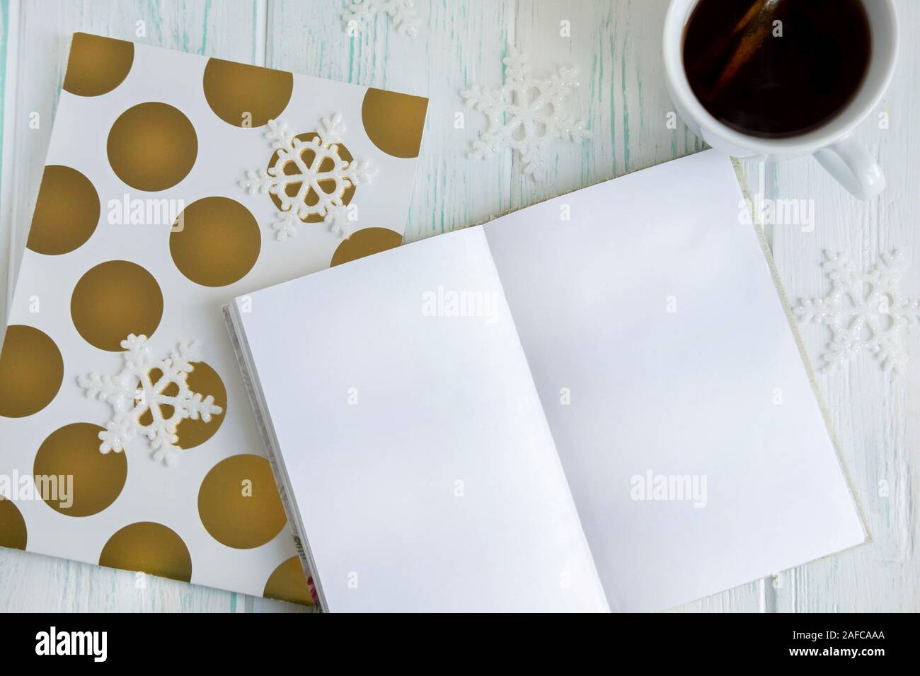 Disposizione del campione di auguri per il nuovo anno con i fiocchi di neve, aprire notebook, tazza di tè su una luce sullo sfondo di legno. Telaio per il testo dei messaggi di saluto per Natale Foto Stock