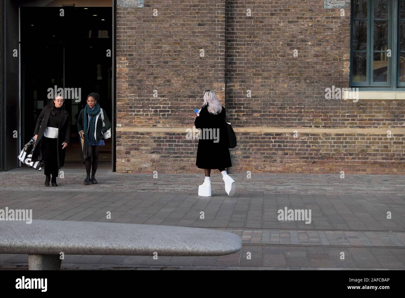 Donna che cammina molto in tacchi alti su bianco stivali fuori Central St Martins Università delle Arti di UAL in Kings Cross Londra Inghilterra KATHY DEWITT Foto Stock