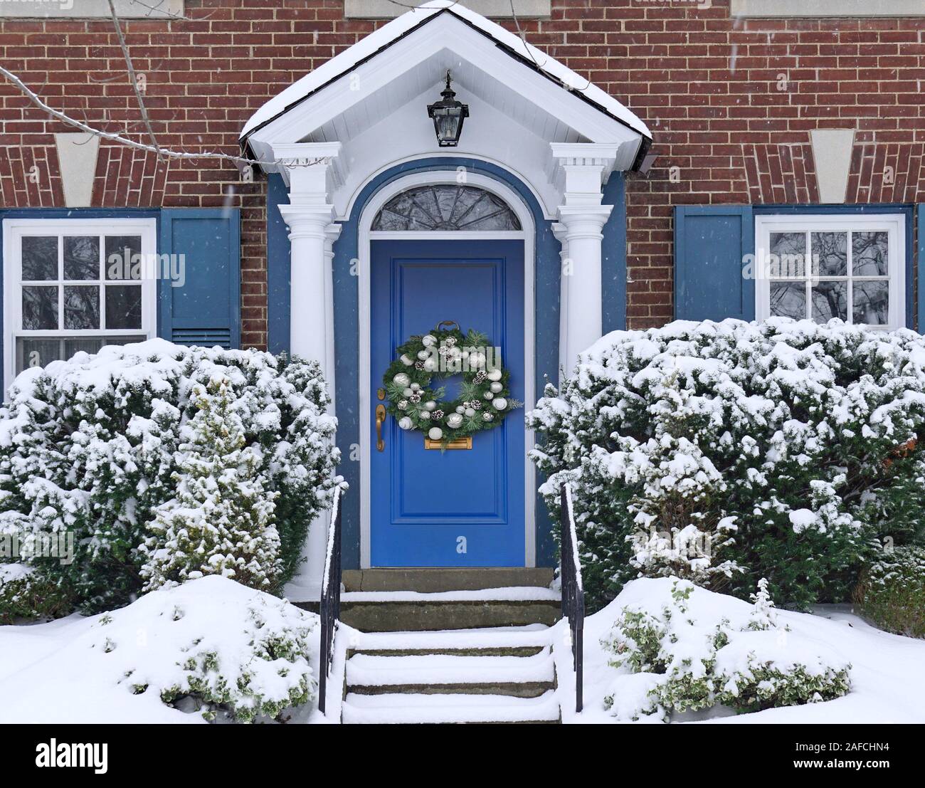 Davanti la porta di casa con la ghirlanda di Natale e coperta di neve pine bush Foto Stock