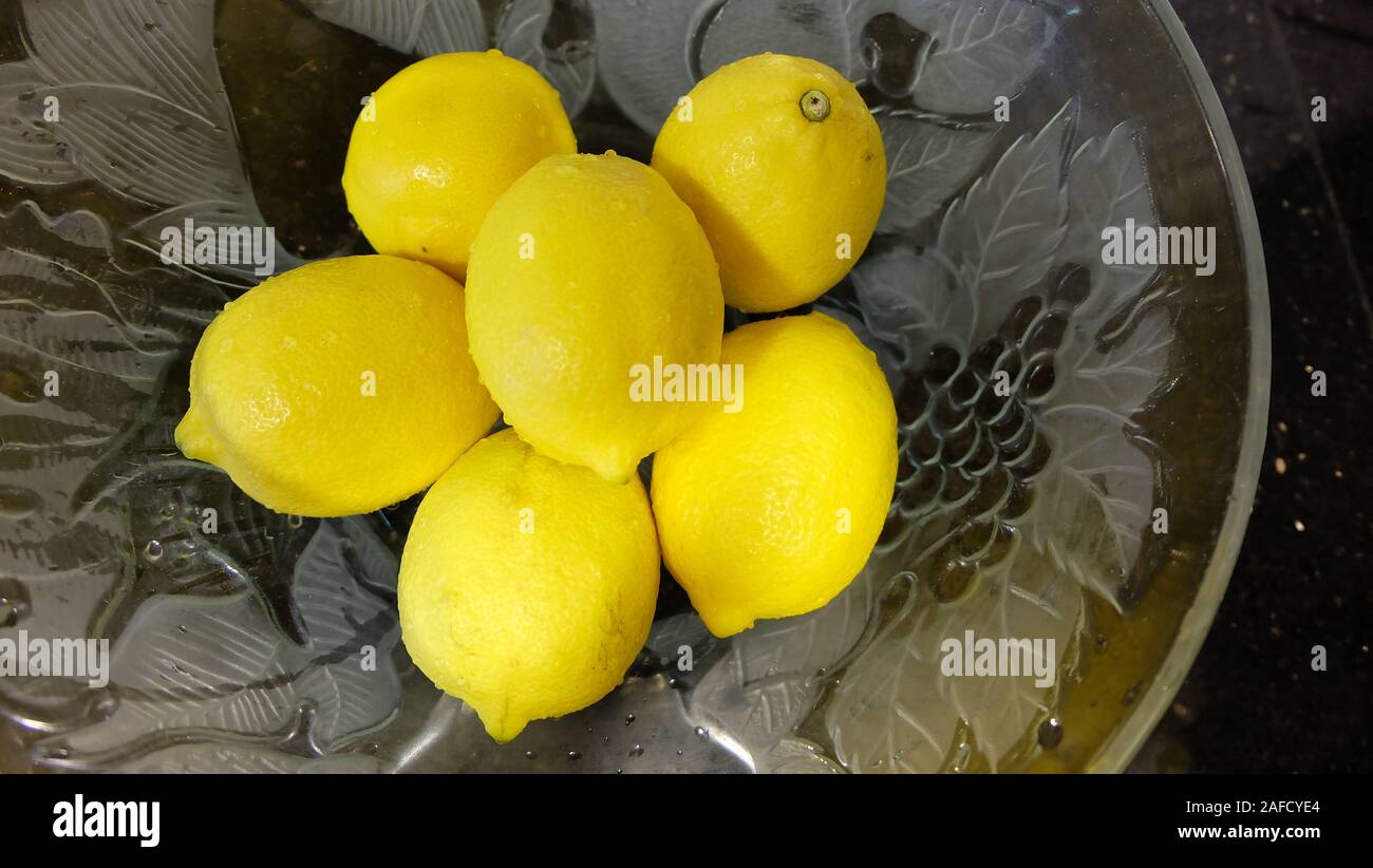 Limoni dentro una grande ciotola di vetro, sulla parte superiore di una superficie nera. Foto Stock