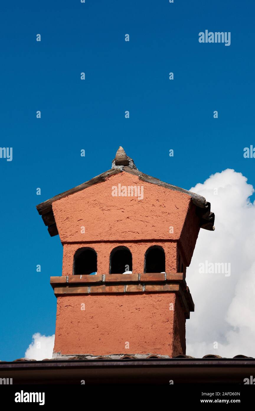 Close-up di un arancione del camino di una casa con tegole di terracotta su un chiaro cielo blu con nuvole. L'Italia, Europa Foto Stock