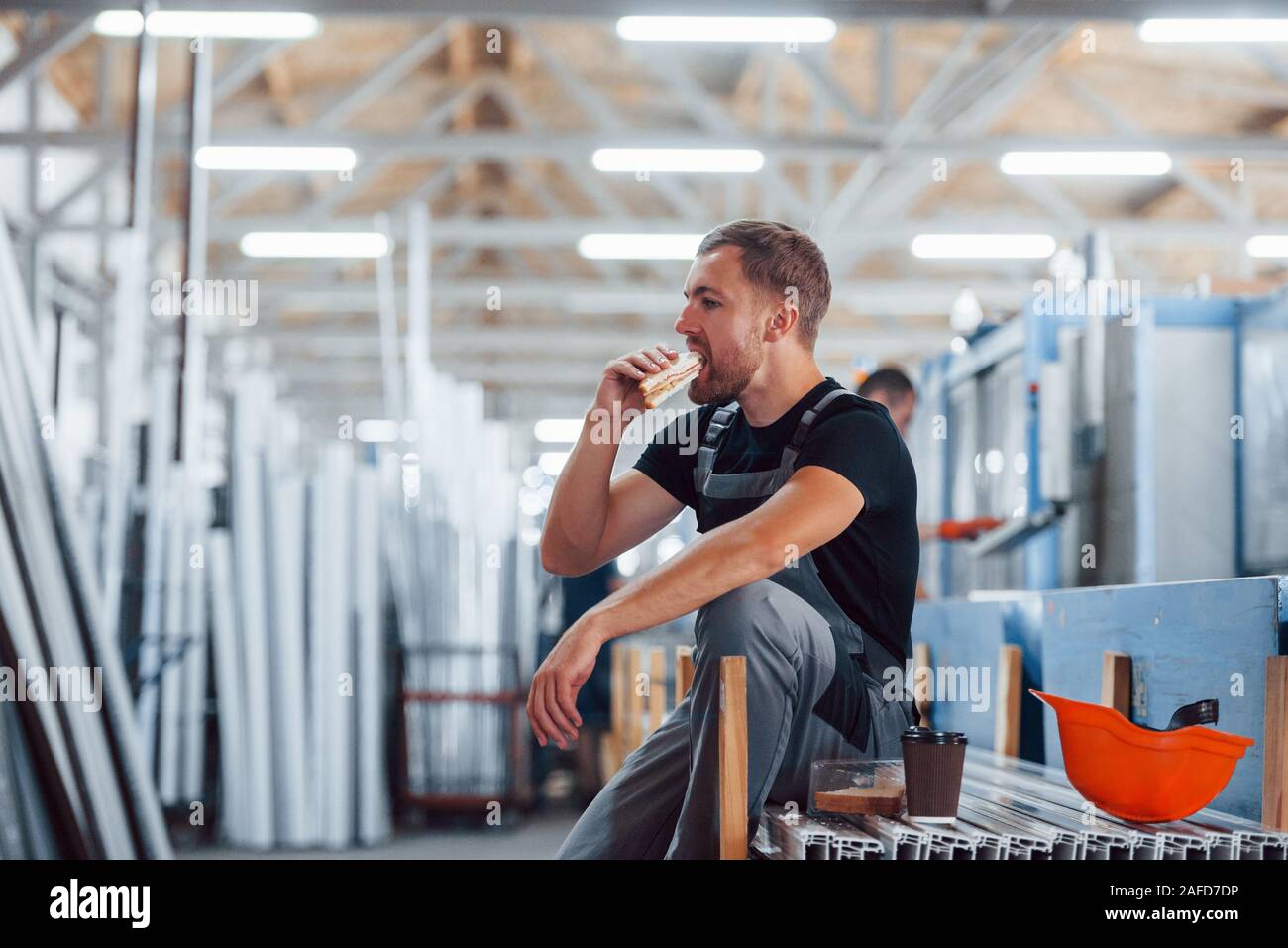 Pausa pranzo. Mangiare e bere. Operaio industriale in ambienti interni in fabbrica. Giovane tecnico con orange elmetto Foto Stock