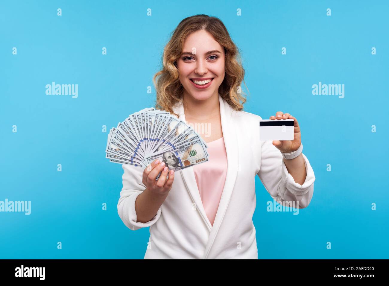 Il settore bancario, cashback. Ritratto di bella donna felice con capelli ondulati in camicia bianca sorridente in telecamera, tenendo la carta di credito e le fatture del dollaro, denaro savi Foto Stock
