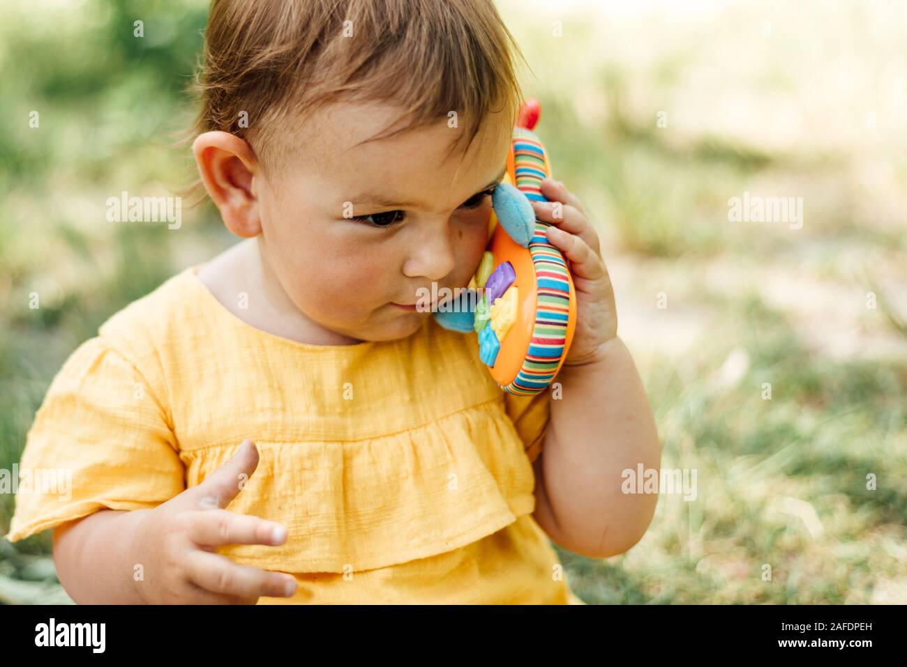 Ragazzina curiosa tramite telefono giocattolo all'aperto nella giornata d'estate. Gen z Foto Stock