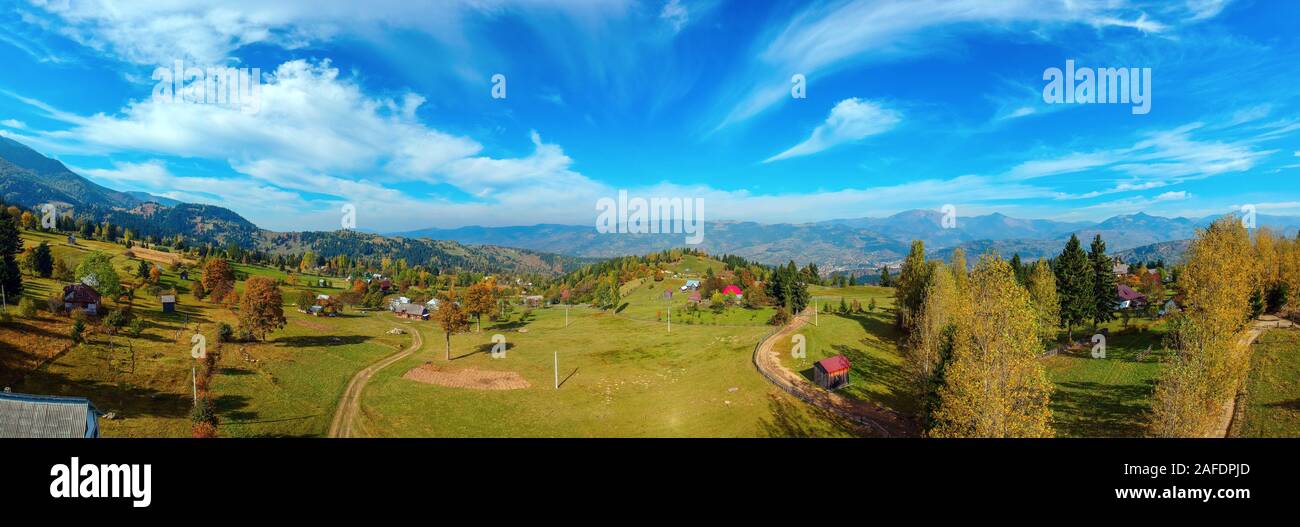 Antenna vista panoramica di una regione rurale con le aziende agricole, campi e montagne dei Carpazi in background in una giornata di sole in autunno. Borsa, Maramu Foto Stock