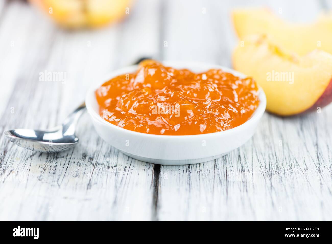 Fatta fresca confettura di pesche (close-up shot; messa a fuoco selettiva) su sfondo di legno Foto Stock