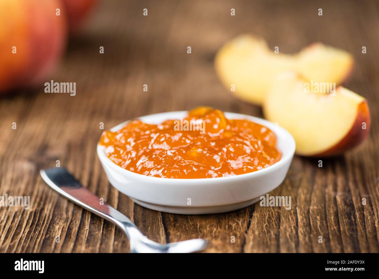 Fatta fresca confettura di pesche (close-up shot; messa a fuoco selettiva) su sfondo di legno Foto Stock