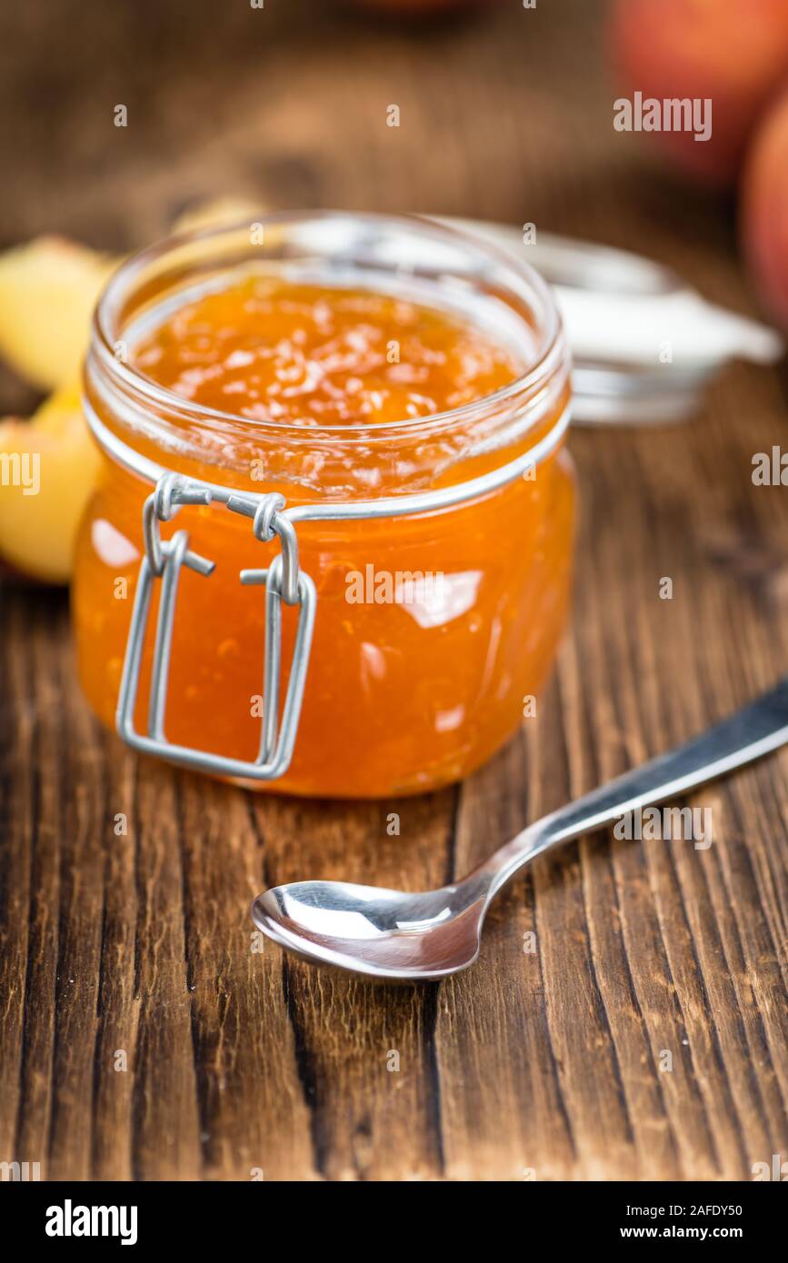 Fatta fresca confettura di pesche (close-up shot; messa a fuoco selettiva) su sfondo di legno Foto Stock