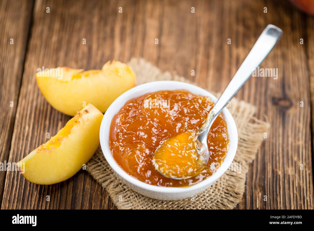 Fatta fresca confettura di pesche (close-up shot; messa a fuoco selettiva) su sfondo di legno Foto Stock