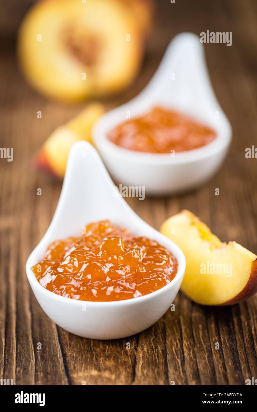 Fatta fresca confettura di pesche (close-up shot; messa a fuoco selettiva) su sfondo di legno Foto Stock
