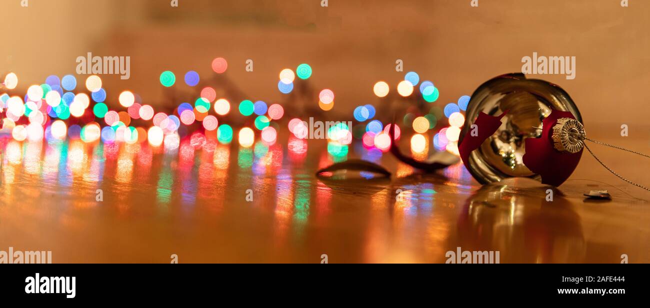 Decorazione per albero di Natale rotto. Vacanze di Natale decorazione, blur luci colorate sfondo incandescente, riflessioni sul pavimento di legno, primo piano, banner Foto Stock