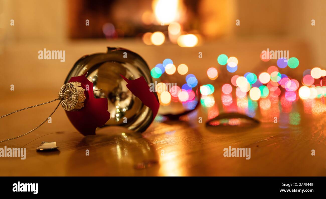 Pallina di natale rotto. Vacanze di Natale decorazione, luci incandescente, blur caminetto a sfondo, riflessioni sul pianale in legno Foto Stock