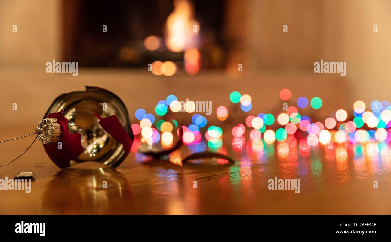 Pallina di natale rotto. Vacanze di Natale decorazione, luci incandescente, blur caminetto a sfondo, riflessioni sul pianale in legno Foto Stock