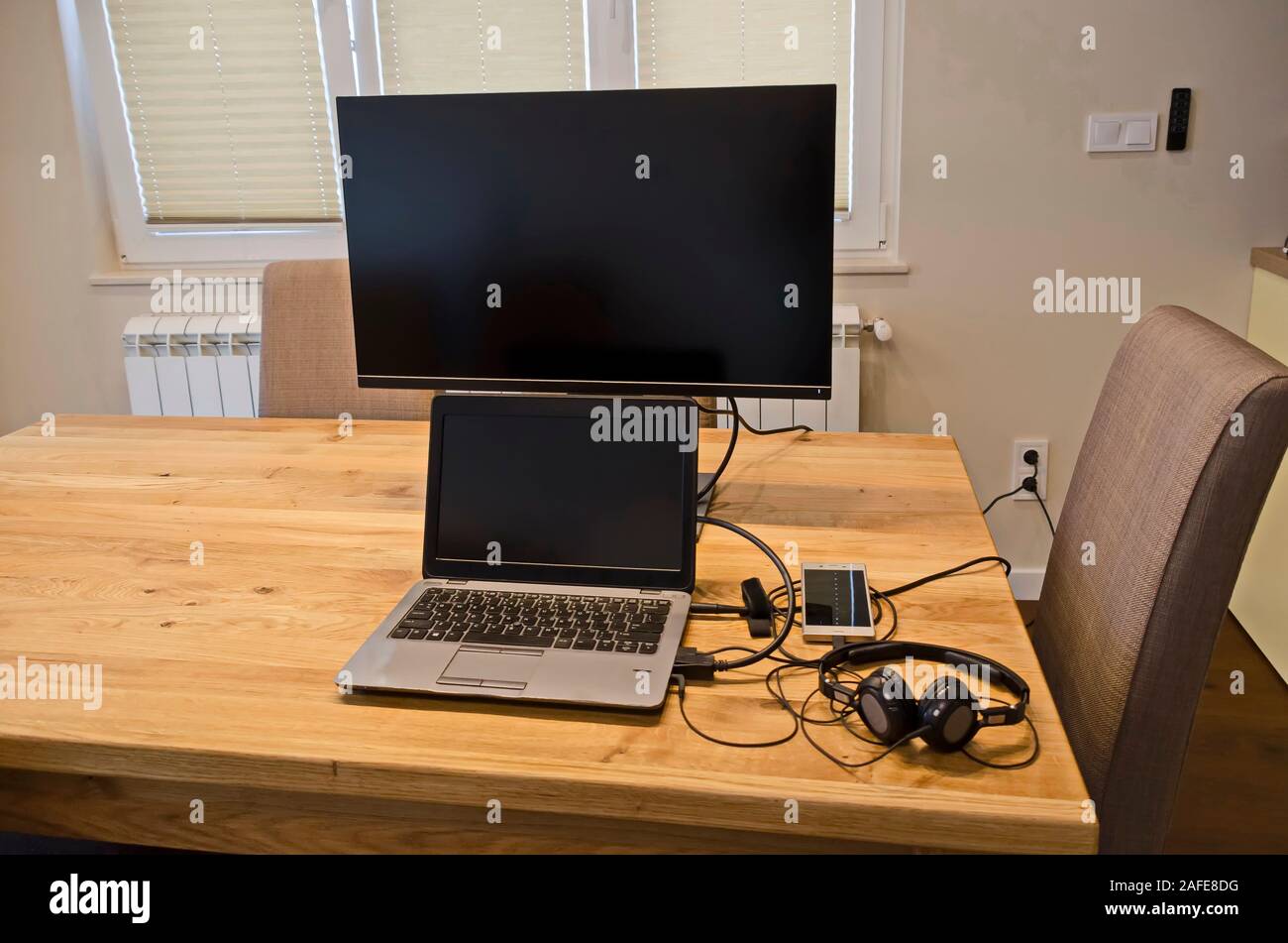 Parte di un tavolo di lavoro con un notebook, monitor, telefono mobile e le cuffie in un rinnovato di recente soggiorno, Sofia, Bulgaria, Europa Foto Stock