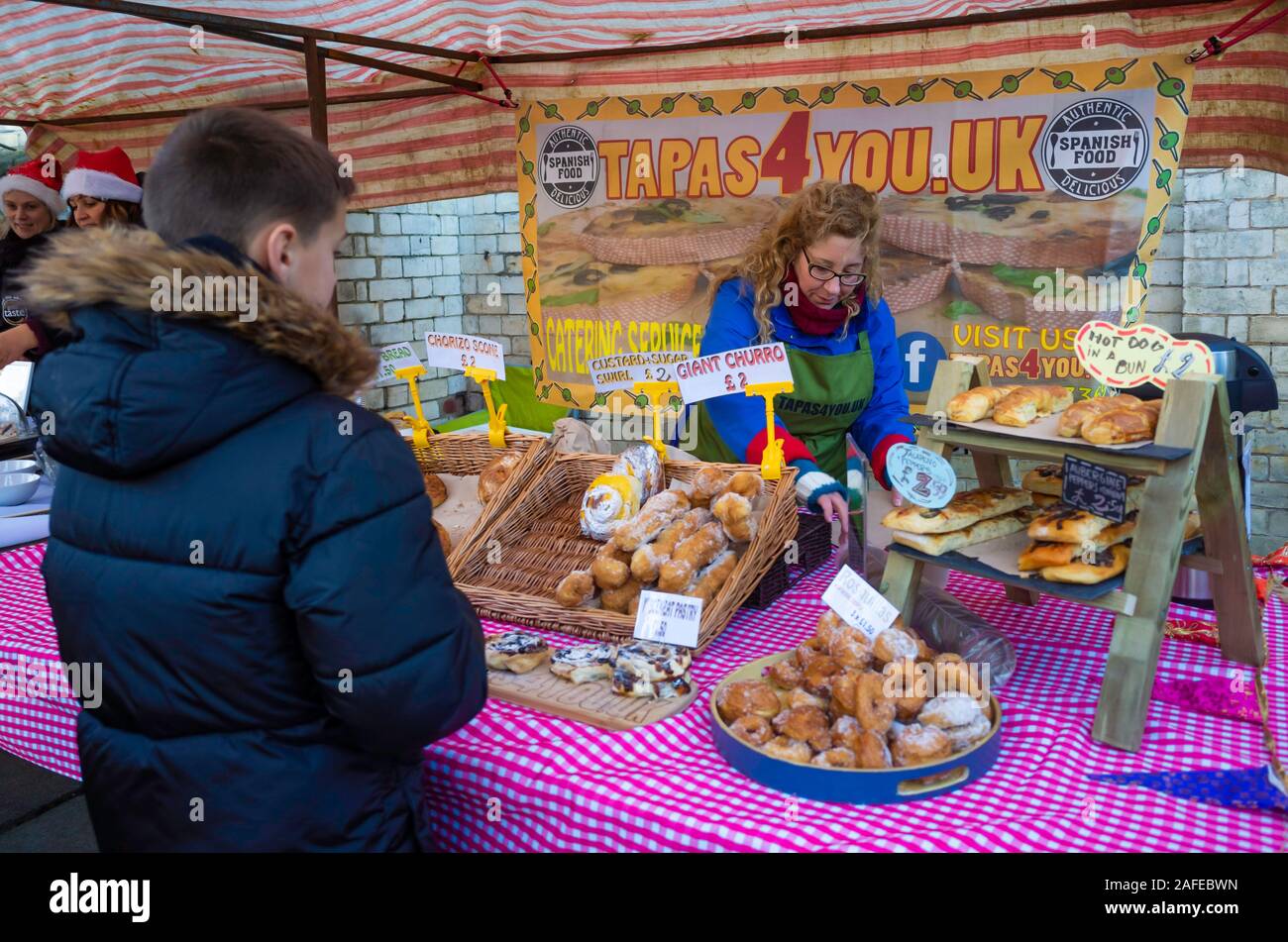 Una donna titolare di stallo ad un agricoltore del Regno Unito il mercato che serve una varietà di tapas spagnole cibo Foto Stock