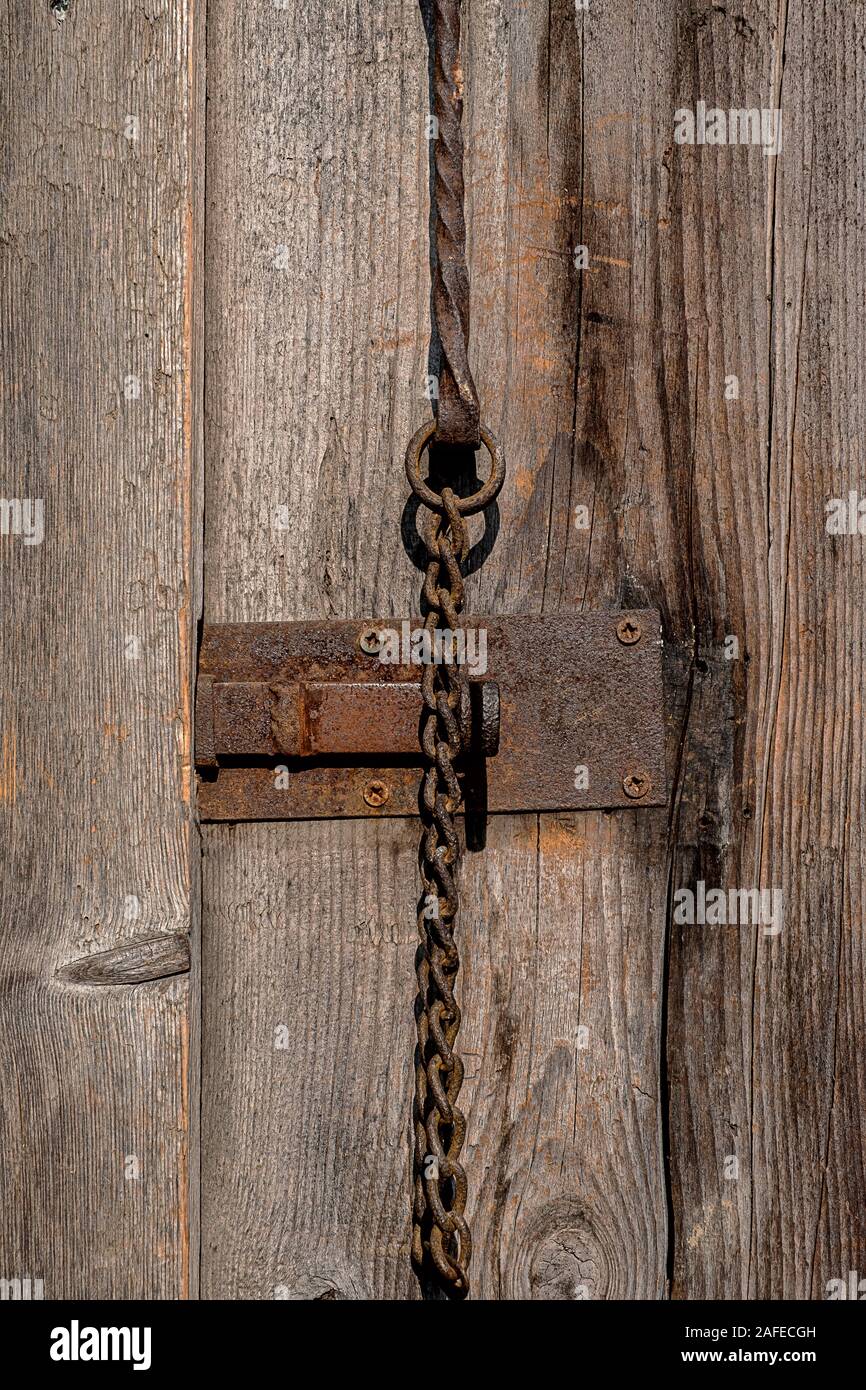 Parte di un antico granaio in legno con porta di ferro arrugginito barra e catena in acciaio Foto Stock