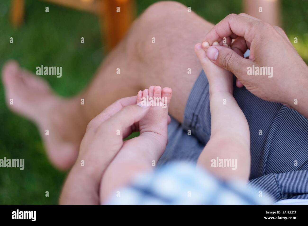 Un uomo è seduto con un bimbo tra le braccia, toccando le piccole gambe Foto Stock