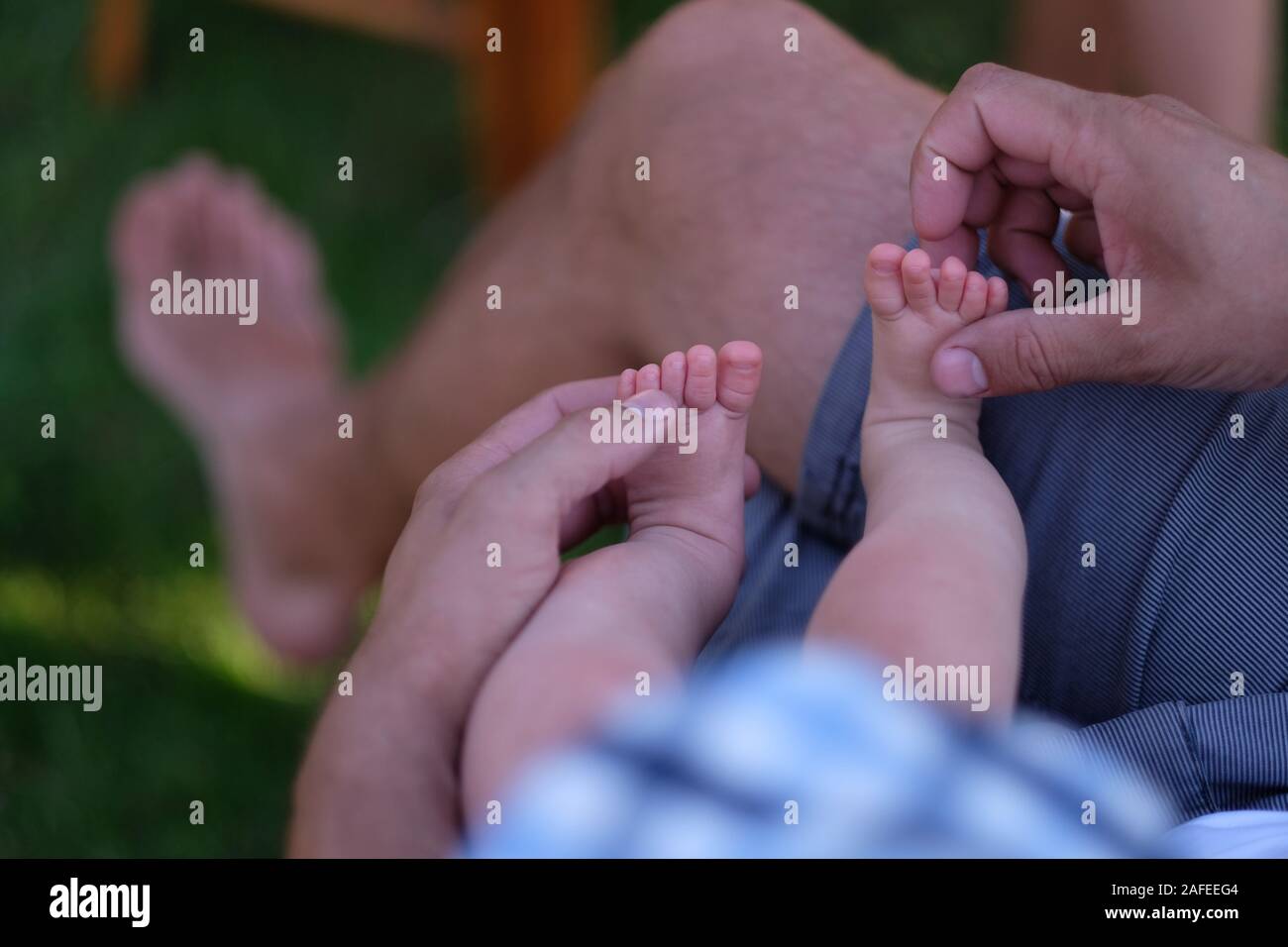 Un uomo è seduto con un bimbo tra le braccia, toccando le piccole gambe Foto Stock