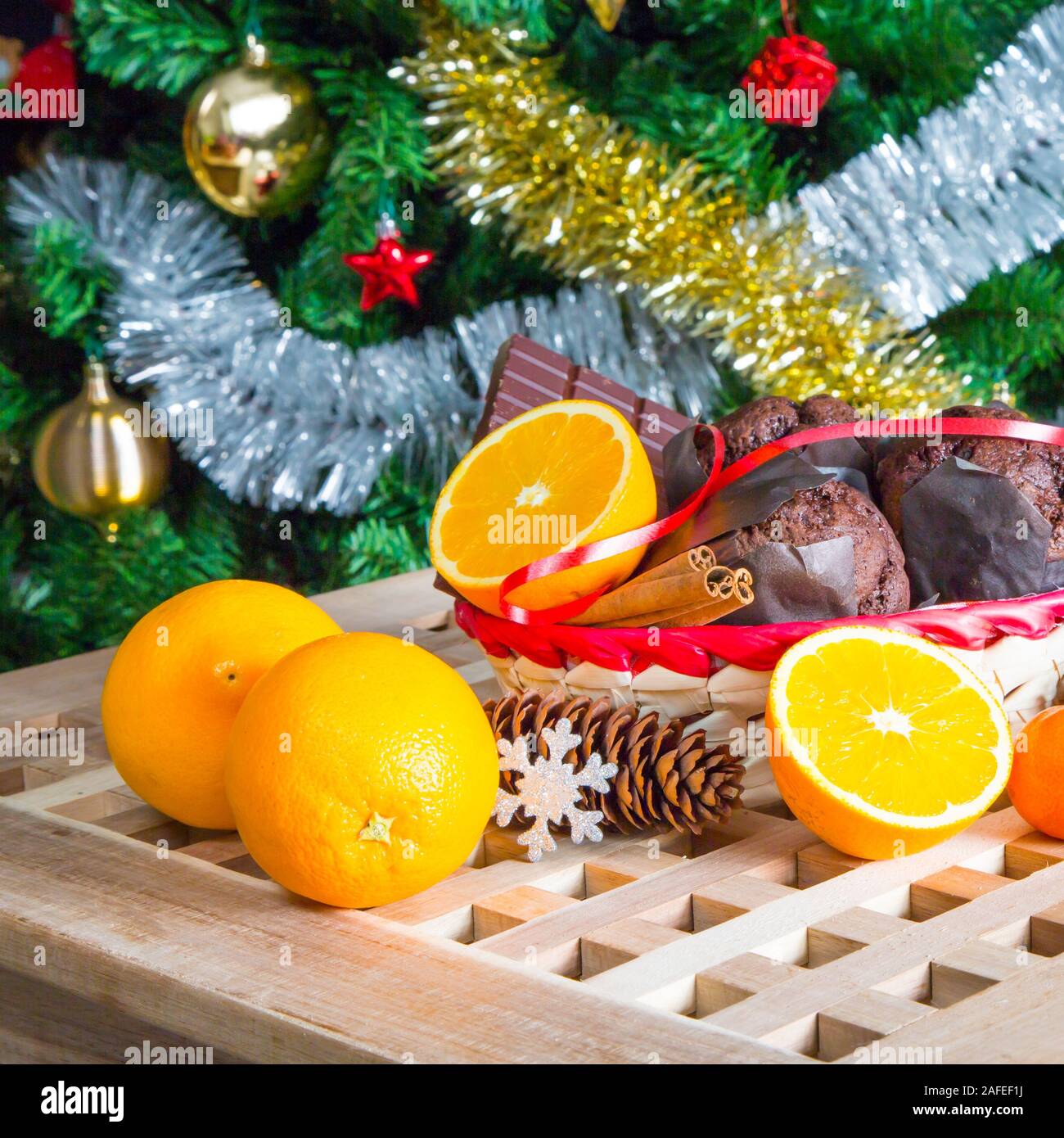 Vacanze di Natale ancora in vita con close up muffin, bastoncini di cannella, arance, cioccolato e cono di pino su albero di Natale sfondo Foto Stock