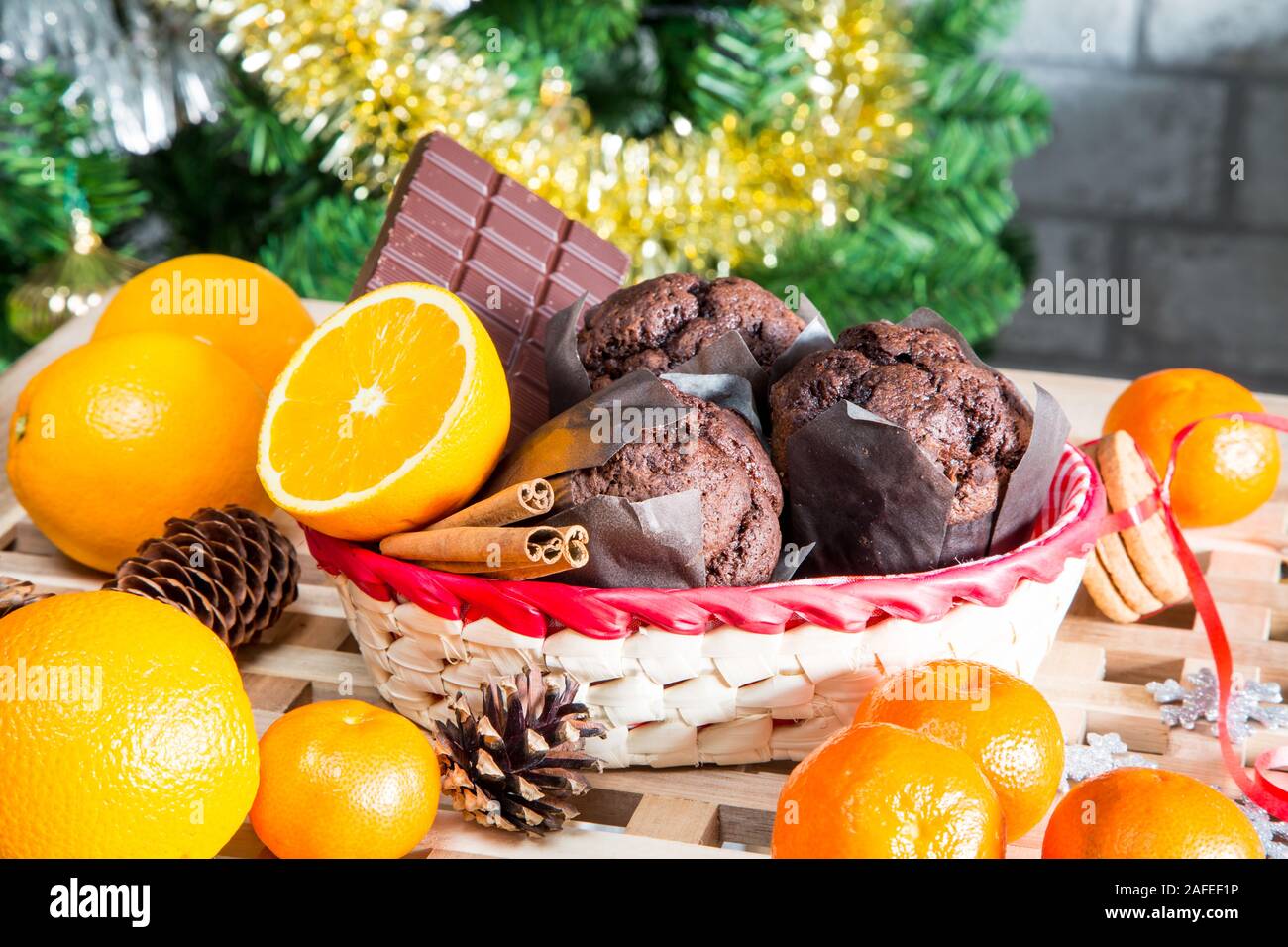 Vacanze di Natale ancora in vita con close up muffin, bastoncini di cannella, arance, cioccolato e cono di pino su albero di Natale sfondo Foto Stock