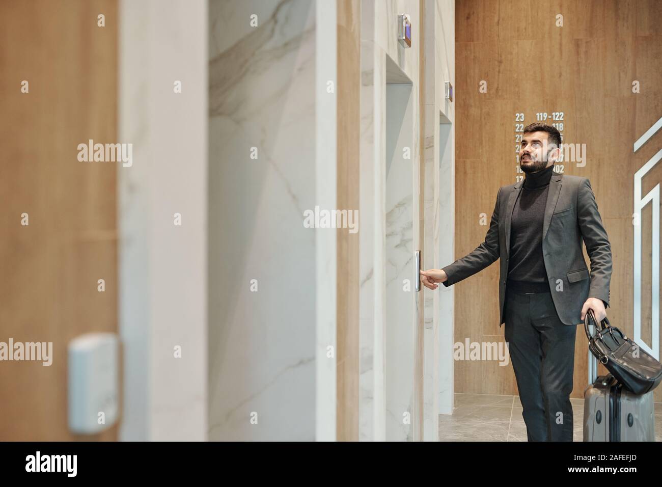 Moderno viaggiatore di affari in tuta elevatore spingendo il pulsante sulla parete Foto Stock