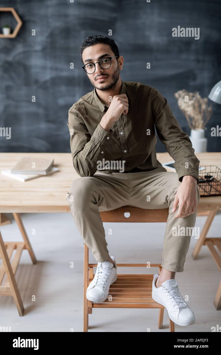 Giovane imprenditore gravi seduti su un tavolo di legno con i piedi sulla sedia che mi Foto Stock
