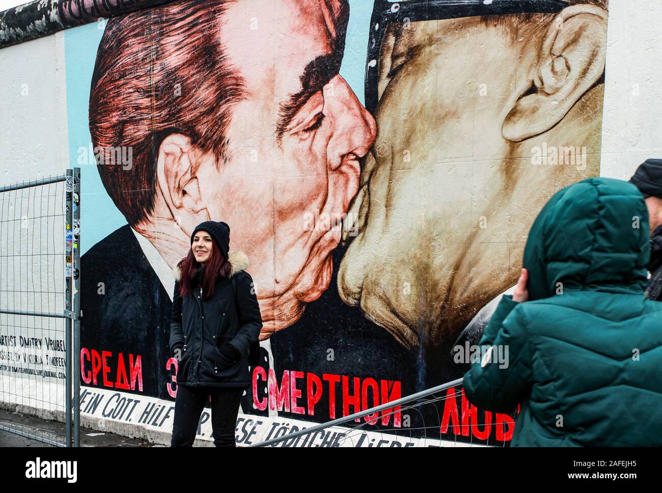 Giovani donne in posa di fronte di Dmitri Vrubel il famoso murale sulla parete di Berlino a East Side Gallery di Berlino, Germania Foto Stock
