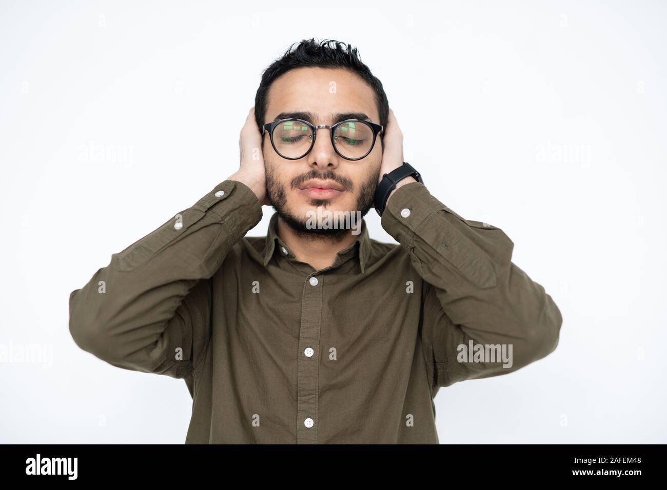 Giovane uomo infastidito in occhiali mantenendo gli occhi chiusi e le mani sulle orecchie Foto Stock