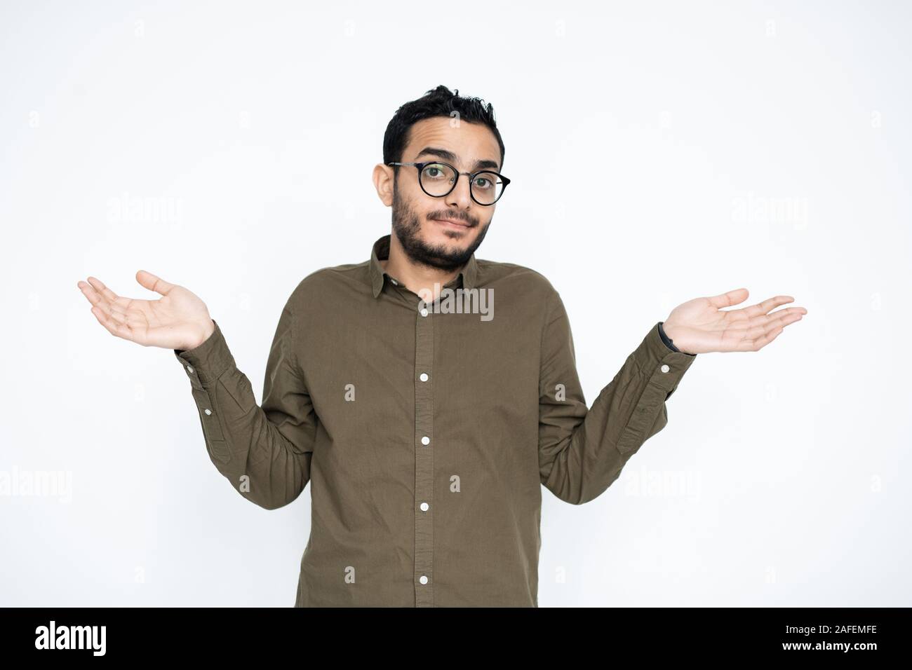 Giovane imprenditore perplesso in occhiali guardando a voi mentre diffondere le sue mani Foto Stock