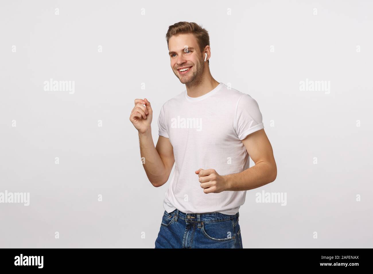 Che un momento quando lyrics colpire voi. Allegra e felice giovane spensierato blon guy dancing, agitando le mani e sorridendo felice, ascoltare la musica in modalità wireless Foto Stock