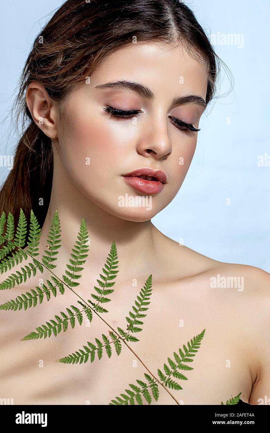 Ritratto di un adulto brunette donna su uno sfondo bianco con verde felce, cura della pelle concetto, una pelle bella e le mani con unghie manicure. Foto Stock