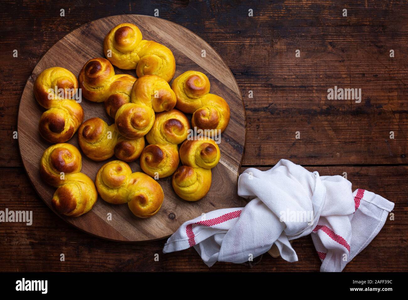 Pane appena sfornato artigianale tradizionale svedese s a forma di ciambelle di zafferano, noto anche come lussebullar o saffransbröd. Visto da sopra il piano giacciono su di un legno scuro Foto Stock