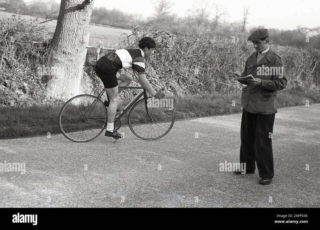 Anni '1950, storico, fuori su una strada di campagna, un ciclista a cronometro che gira in giro per un cronometro ufficiale sul campo, Inghilterra, Regno Unito. In una cronometro un ciclista gareggia contro il cronometro per ottenere il pareggio più veloce. Foto Stock