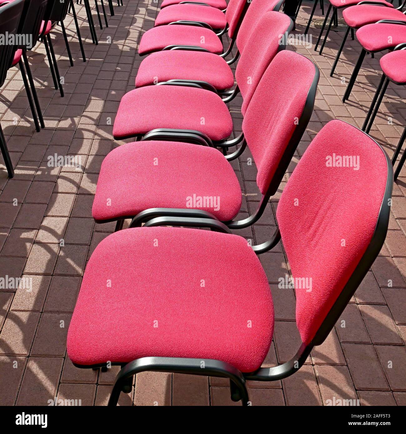 Righe vuote di sedie da ufficio con soluzione satura di colore rosso cremisi dei sedili si trovano sul marciapiede all'aperto in estate le giornate di sole durante il festival Foto Stock