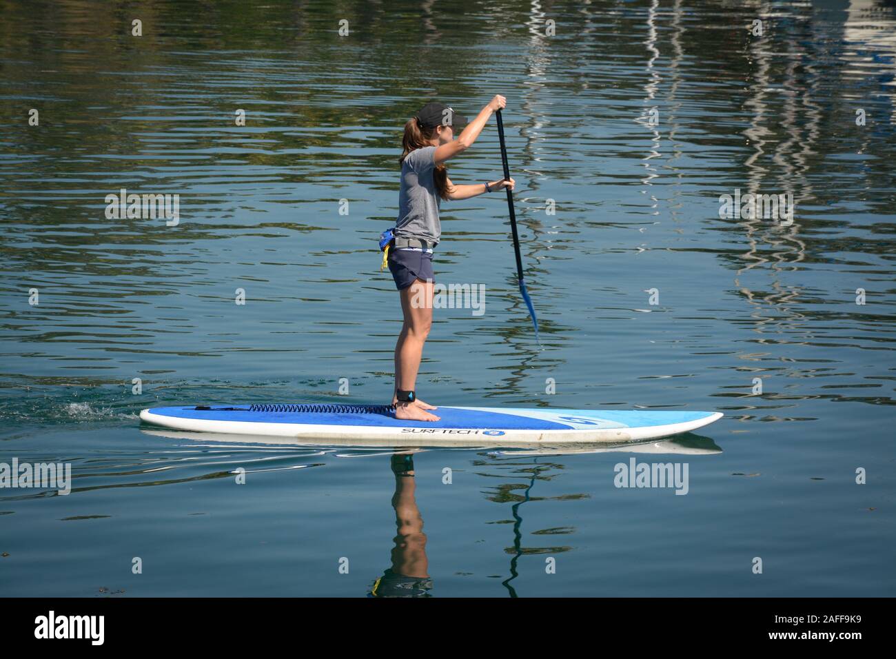 Vista laterale di una giovane donna pagaiando su uno stand up paddle in pensione il Santa Barbara canale nel porto di Santa Barbara, CA, Stati Uniti d'America, Foto Stock
