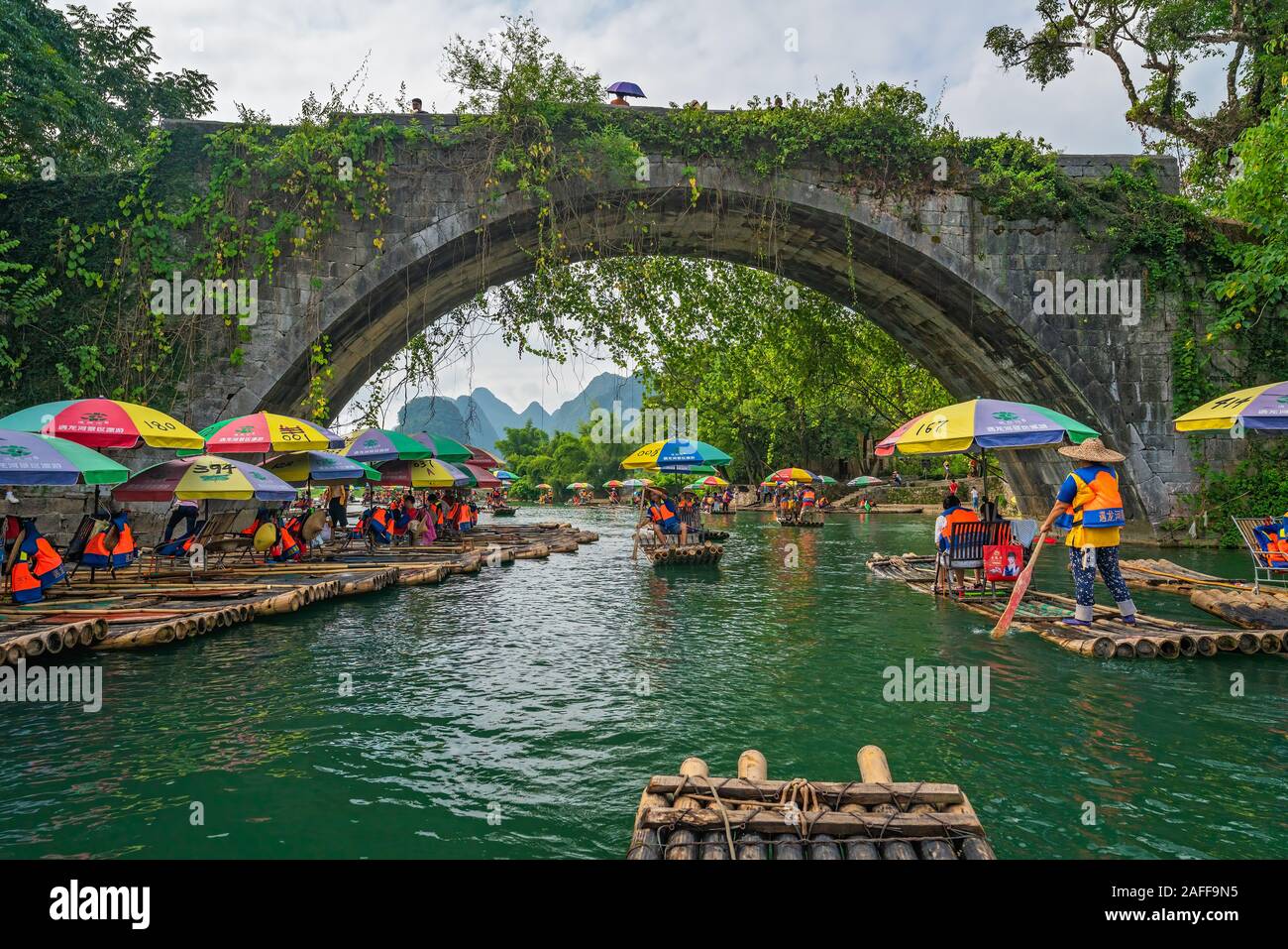 Yangshuo, Cina - Agosto 2019 : piccolo locale di trasporto turistico di passeggeri imbarcazioni di bambù di trasporto persone sotto la storica Yulong Qiao ponte sul viaggio lungo th Foto Stock