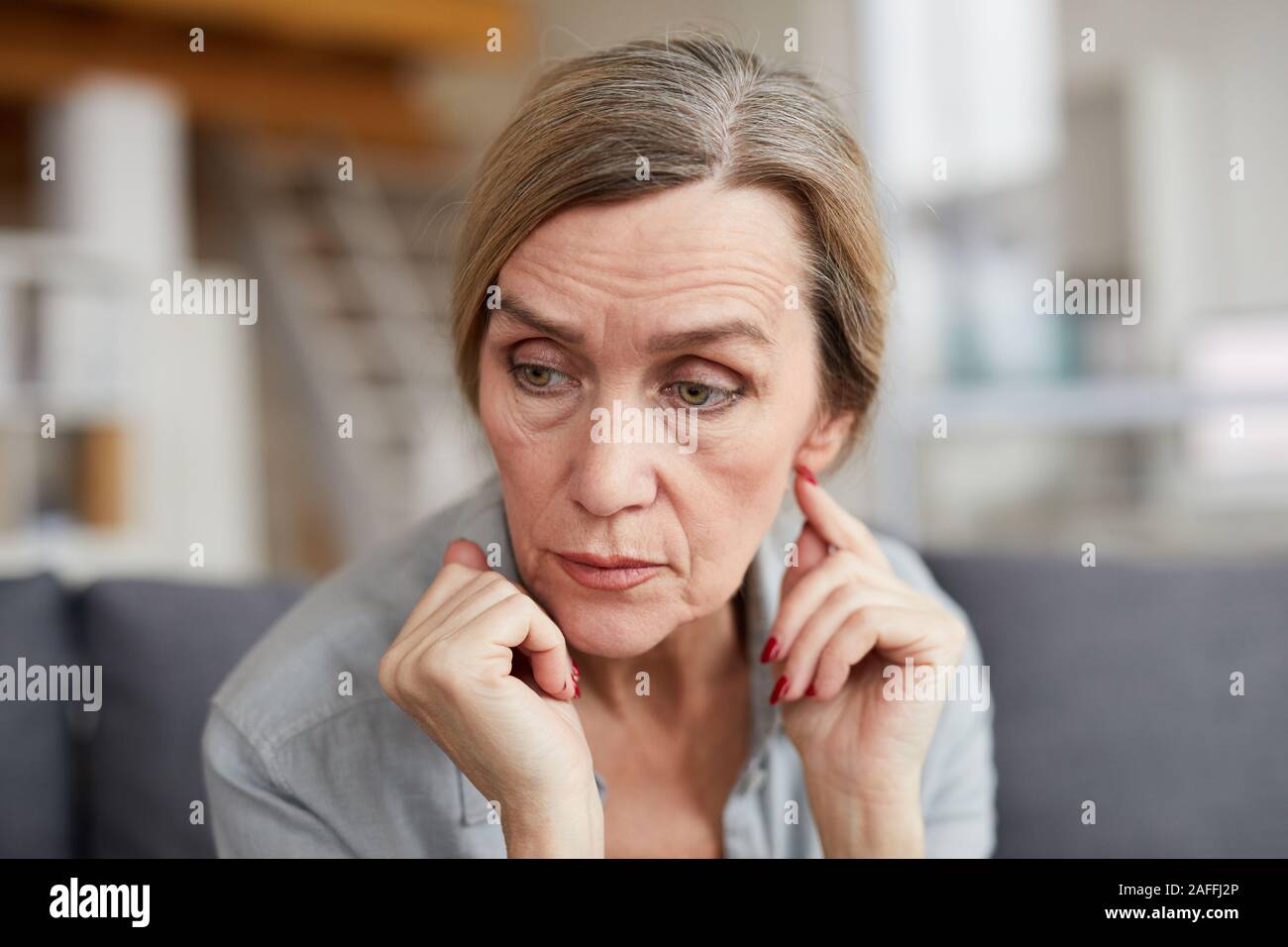 Ritratto di triste donna matura seduti sul divano di casa e guardando lontano con preoccupazione e ansia, spazio di copia Foto Stock