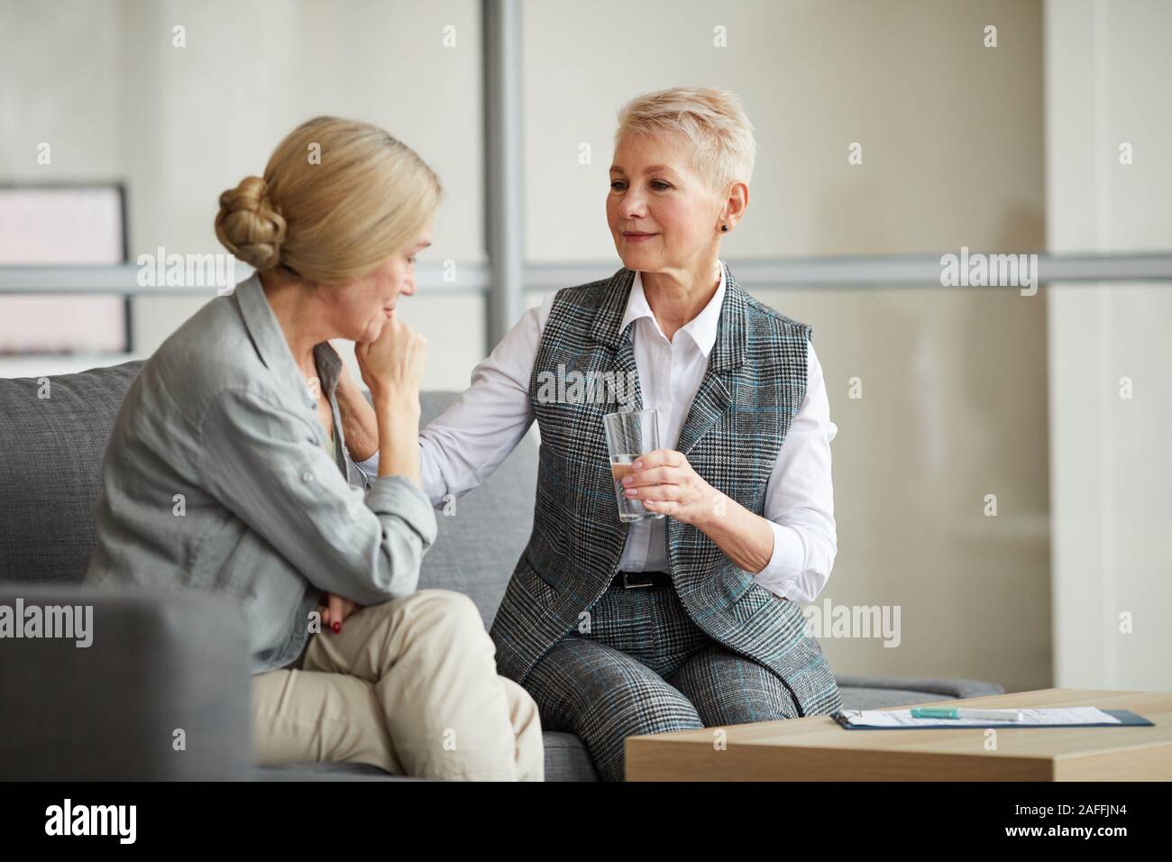 Ritratto di cura psicologo femmina che offre un bicchiere di acqua per piangere donna senior mentre la sua consolante durante la sessione di terapia, spazio di copia Foto Stock
